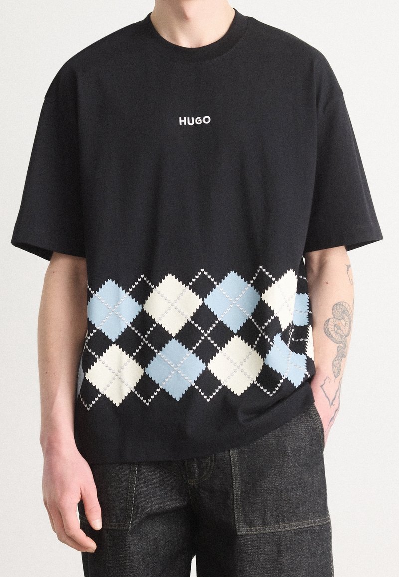 Schwarzes Baumwoll-T-Shirt mit einem weißen "HUGO"-Logo und einem mehrfarbigen Rautenmuster in Blau, Weiß und Schwarz im unteren Bereich.