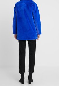 Blå fuskpälsjacka med en lös passform, bred krage och långa ärmar, kombinerad med svarta tajta byxor och ankelboots.