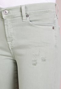 Vihreät farkut, jotka on valmistettu denimistä, slim fit -mallilla, hieman kulutettuina ja hopeisilla yksityiskohdilla vyötäröllä ja taskuissa.