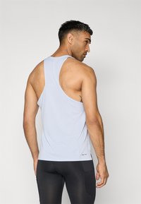 Helle blaue ärmellose Tanktop mit Racerback-Design, aus atmungsaktivem Stoff, mit subtiler Textur und einem kleinen Etikett am Saum.