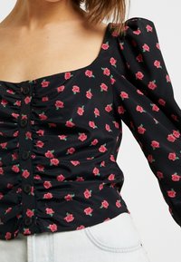Blusa nera floreale con scollatura quadrata, maniche a palloncino e tessuto arricciato. Presenta una stampa di fiori rosa e chiusura con bottoni frontali.