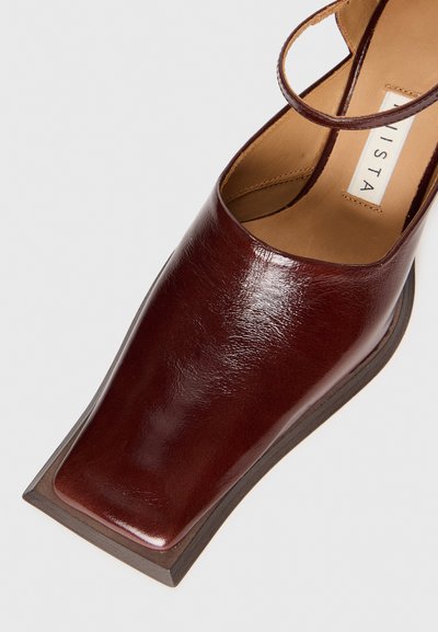 Tacco in pelle bordeaux con design a punta quadrata, superficie liscia e dettaglio della fascia minimalista, dotato di una soletta marrone texturizzata.