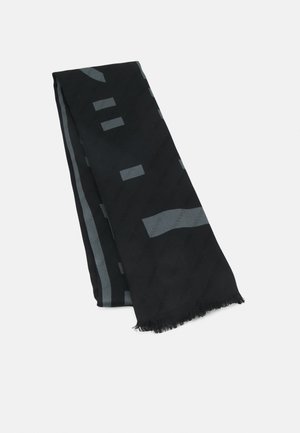 Écharpe noire avec motifs géométriques abstraits gris et bords frangés, pliée sur un fond blanc.