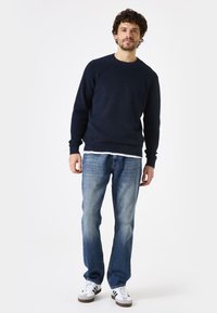 Marineblauwe gebreide trui met lange mouwen, gecombineerd met lichtblauwe rechte jeans en witte sneakers met zwarte accenten.