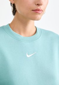 Mintgroene sweatshirt met een geribbelde halslijn en een wit Nike-logo op de borst. Zachte textuur, eenvoudig ontwerp, geen patronen of aanvullende details.
