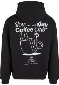 Sweat à capuche noir avec un graphisme blanc représentant une personne se relaxant dans une tasse de café et un texte indiquant "Slow Sunday Coffee Club" ainsi que des petites phrases motivantes.