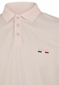 Polo-shirt rose clair en tissu texturé, col boutonné, et logo "HECHTER" brodé avec des accents rouge, blanc et bleu.