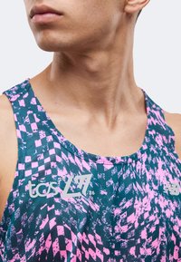 Gros plan d'une personne portant un haut de sport sans manches avec un motif abstrait bleu et rose et des logos sur la poitrine.