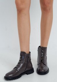 Stivaletti alla caviglia in pelle verniciata grigia con suola robusta e dettagli decorativi a cerniera sui lati. Texture liscia e design elegante.