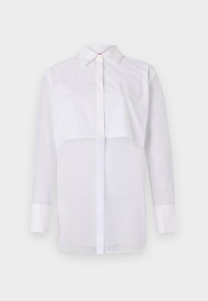 Valge pika varrukaga pluus kerge kangaga, klassikalise krae, eesnööbid ja kihiline disain, millel on läbipaistev alumine osa.