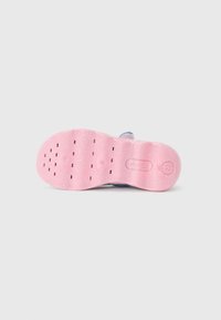 Suela de zapato flexible en goma rosa con agujeros de drenaje, superficie texturizada y sutil logotipo de la marca, con un material superior azul suave.