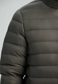 Mørkegrøn pufferjakke med quiltet design, glat tekstur, høj krave og syede vandrette sømme til isolering.