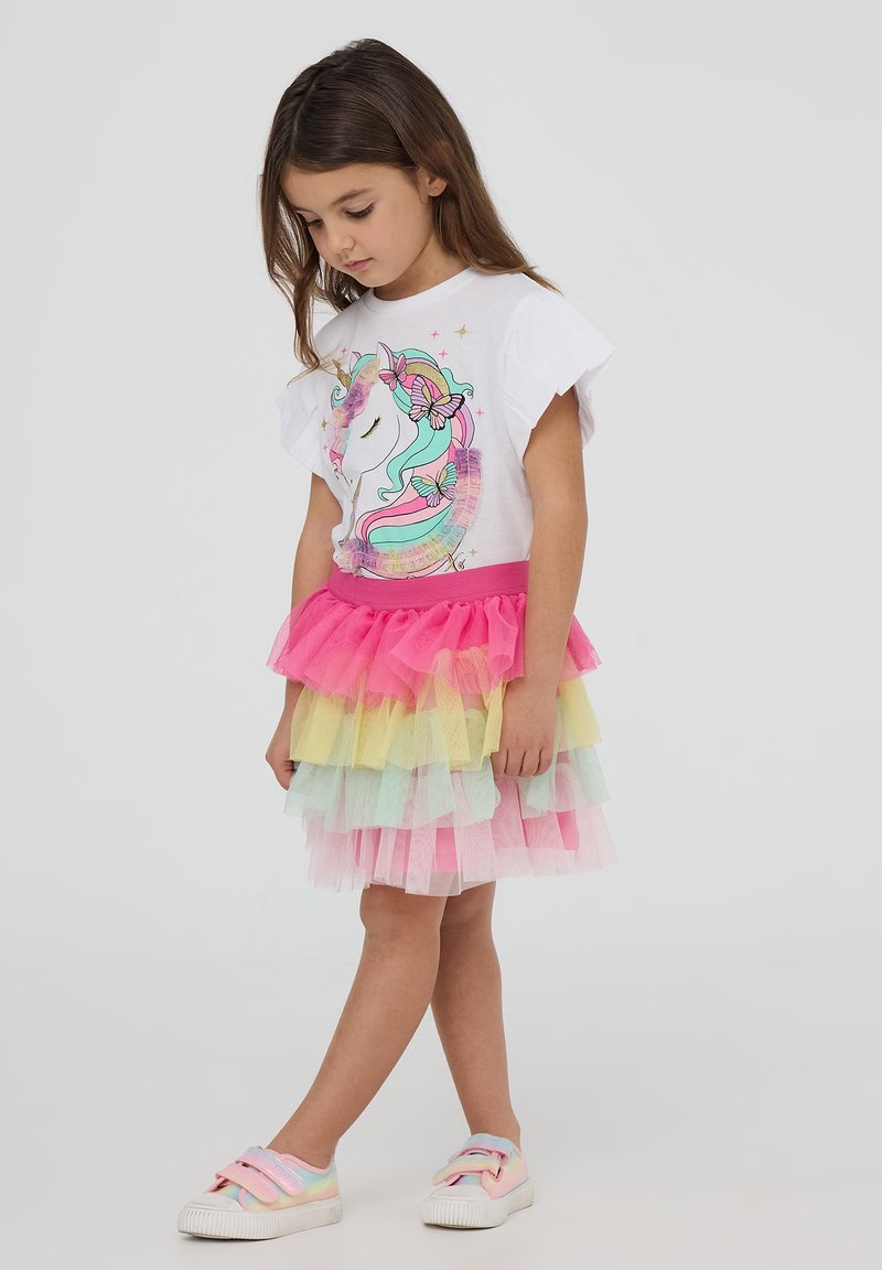 T-shirt bianco con grafica di unicorno e dettagli a forma di farfalla, abbinato a una gonna di tulle multicolore con strati rosa, giallo e verde.