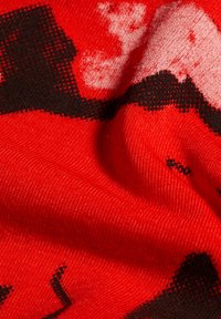 Röd stickad tyg med en mjuk textur, med ett mönster av svarta och vita former. Materialet verkar töjbart och slätt.