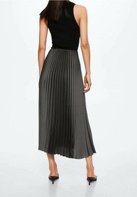 Top negro sin mangas combinado con una falda gris plisada de longitud media. La tela parece suave, con pliegues verticales y una silueta fluida.