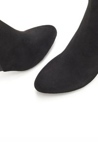 Botas de tobillo negras de ante con puntas afiladas, que presentan una textura suave y un diseño ajustado. Sin herrajes ni acentos visibles.