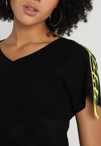 Haut en maille noire tricotée à manches courtes. Doté d'un décolleté en V et de détails de bretelles jaunes vifs le long de l'épaule, ajoutant un élément de contraste.