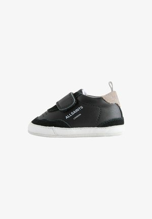 Zapatilla infantil en blanco y negro con cierre de velcro, detalles en ante y texto "ALLSAINTS LONDON" en el lateral.