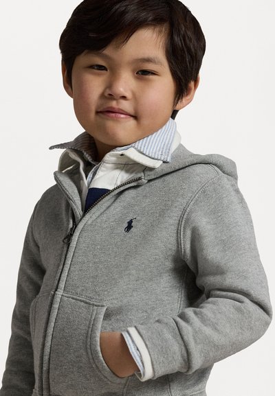 Graue Reißverschluss-Hoodie mit Taschen, versehen mit einem dunkelblauen Polo-Logo. Darunter ein Hemd mit Kragen im blau-weiß gestreiften und karierten Muster.