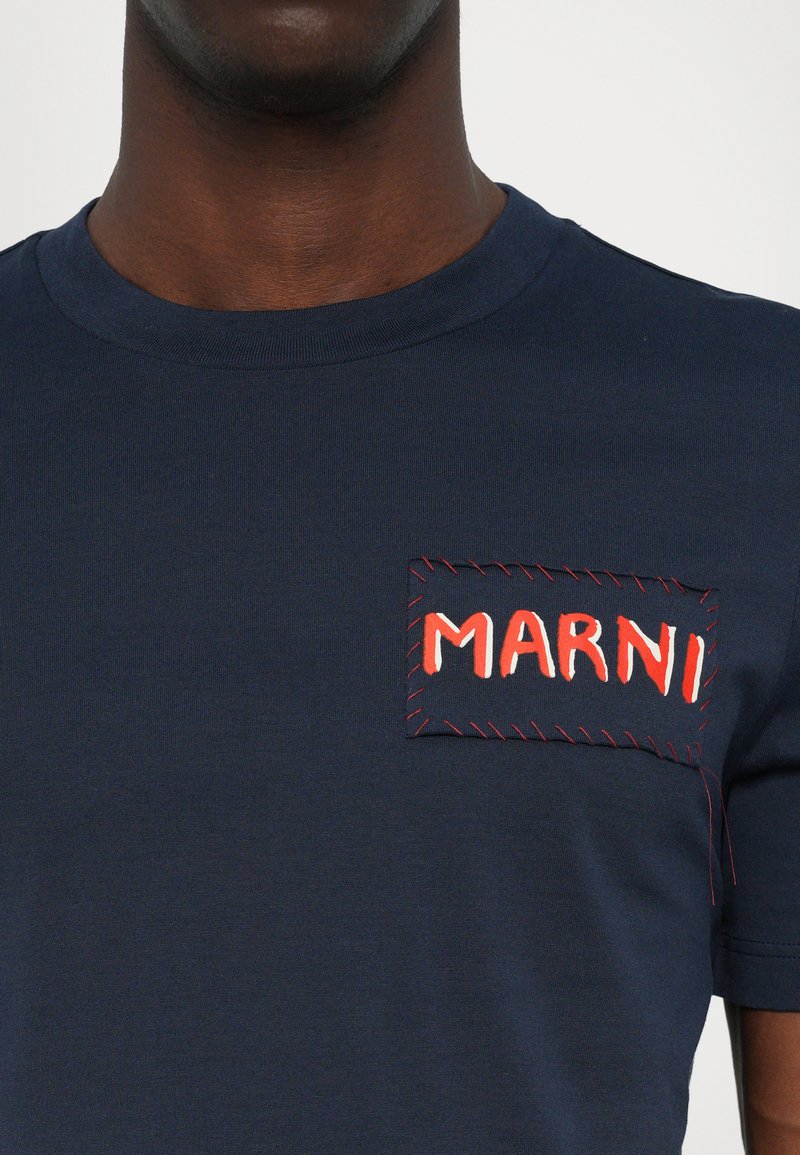 Camiseta de algodón azul marino con un parche rectangular bordado que lleva la palabra "MARNI" en rojo y blanco, acentuado por costuras rojas.