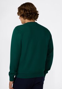 Sudadera verde oscuro con cuello redondo, puños y dobladillo acanalados. Textura suave sin patrones ni logotipos visibles.