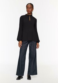 Blusa nera a coste con maniche lunghe a sbuffo e scollatura a oblò, abbinata a pantaloni in denim scuro a gamba larga con vita alta.