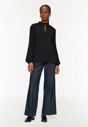 Blusa nera a coste con maniche lunghe a sbuffo e scollatura a oblò, abbinata a pantaloni in denim scuro a gamba larga con vita alta.