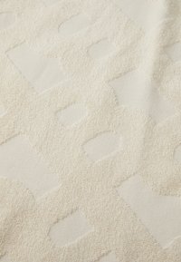 Tessuto beige testurizzato con un motivo geometrico in rilievo caratterizzato da anelli e curve, che crea una superficie tattile con profondità variabili.