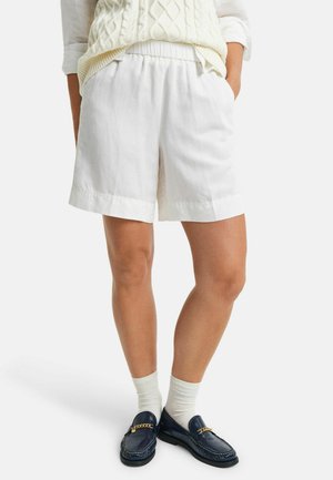 Witte linnen shorts met een elastische tailleband, voorzien van een losse pasvorm en omgeslagen zomen, gecombineerd met donkere loafers en crèmekleurige sokken.