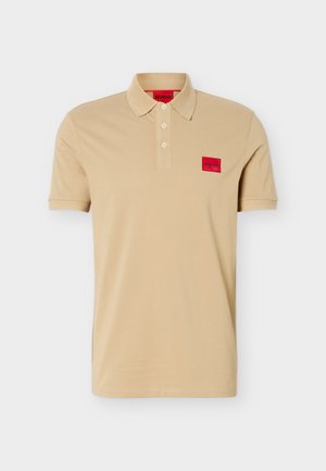 Bež kratka polo majica s tri gumba, rebrastim ovratnikom i manžetama te crvenim logotipom "HUGO" na prsima i unutarnjem dijelu ovratnika.