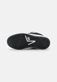 Black athletic shoe sole featuring a textured rubber surface, a prominent logo, and a curved design with traction patterns.
