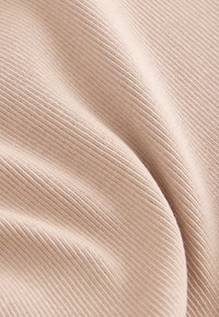 Tissu beige clair côtelé avec une texture douce, présentant une apparence ondulée et de fines lignes verticales créant un motif uniforme.