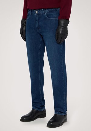 Jeans in denim blu scuro con un taglio dritto, caratterizzati da una chiusura con bottone argentato, tasche laterali, indossati con guanti in pelle nera e stivali.