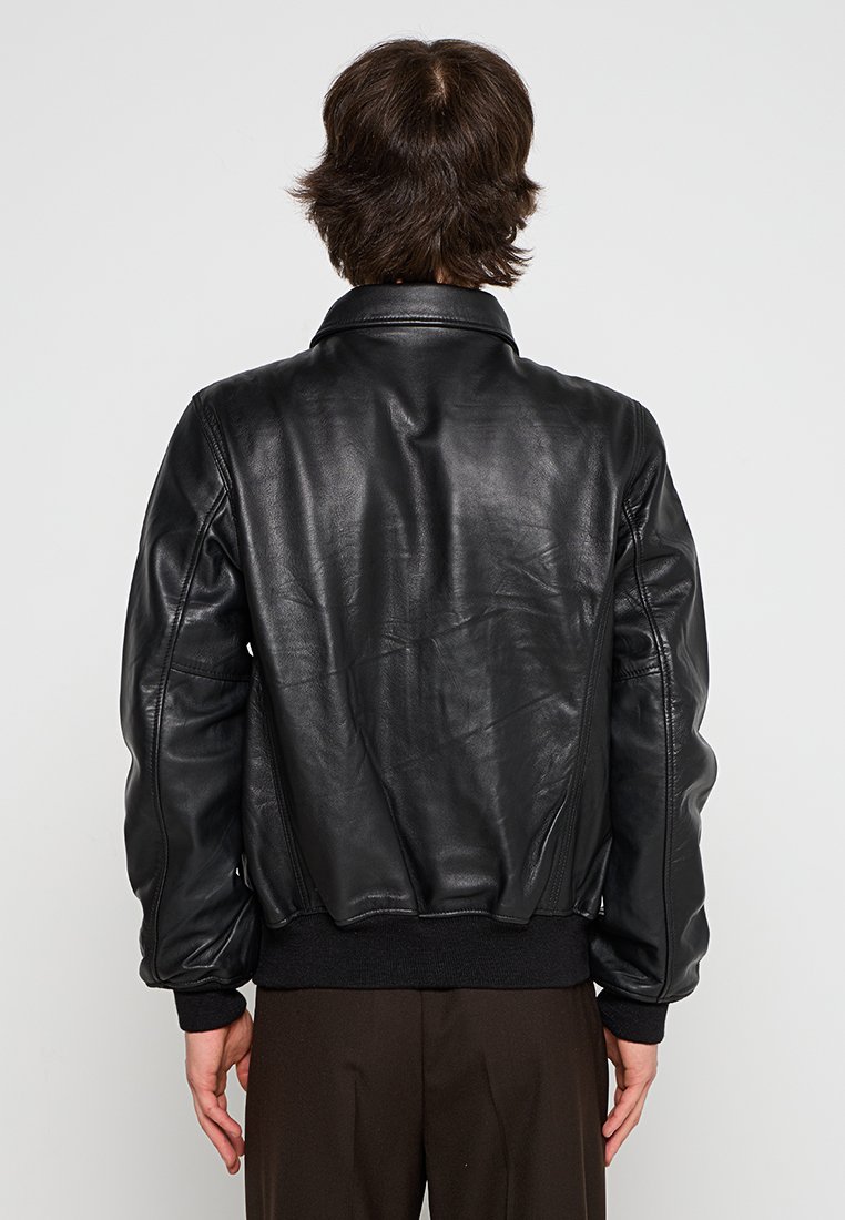 Veste en cuir noir de style aviateur avec un ourlet et des poignets en maille côtelée, dotée d'une texture lisse et d'un design de col classique.