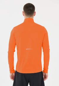 Miesten pitkähihainen urheilupaita, kirkkaan oranssi, teksturoitu kangas, korkea kaulus, heijastava yksityiskohta selässä, slim fit -muotoilu.