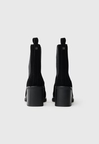 Μαύρες σουέτ μπότες έως τον αστράγαλο με χαμηλό τακούνι, ελαστικές πλευρικές επενδύσεις και θηλιές για εύκολη εφαρμογή. Ο σχεδιασμός είναι κομψός με υφή.