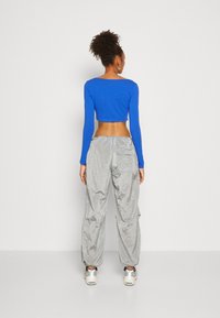 Blå långärmad crop top med vid halsringning, parat med grå, skrynkliga, löst sittande byxor med fickor och elastiska muddar.