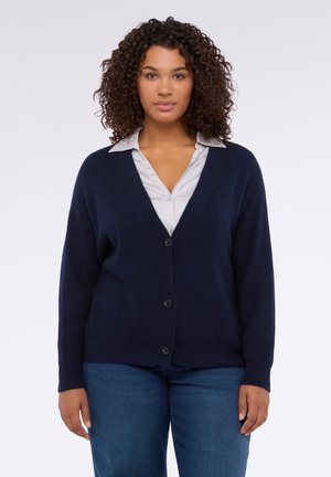 Cardigan blu navy con motivo a maglia strutturata, scollo a V, maniche lunghe e cinque bottoni frontali, indossato sopra una camicia con colletto.