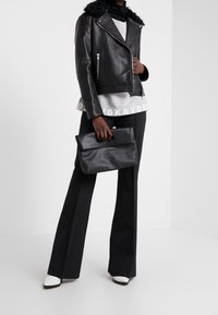 Giacca da moto in pelle nera con colletto in pelliccia sintetica, felpa grigia con testo, pantaloni neri a gamba larga e pochette nera con manico.