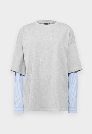 Camiseta gris de gran tamaño con mangas cortas, que presenta un diseño en capas con mangas largas a rayas azules y blancas por debajo.