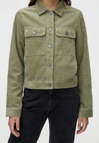 Veste en velours côtelé vert olive avec deux poches poitrine, fermeture à boutons et ourlet côtelé. Comprend des manches longues et un col.