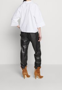 Camicia bianca, leggera e comoda con maniche arrotolate, abbinata a pantaloni di pelle nera e stivali con tacco in suede marrone. Vista posteriore dell'outfit.