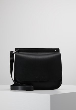 Black leather crossbody bag with a flap closure and adjustable strap, displayed on a white pedestal against a plain gray background.