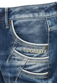 Blaue Jeans aus Denim mit einem verwaschenen Finish; verfügt über ein einzigartiges genähtes Taschendesign und kontrastierende weiße Akzente. "CIPO&BAXX" Logo in der Nähe der Taschen.