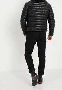 Zwarte pufferjack met doorgestikte textuur en capuchon, gecombineerd met zwarte jeans en enkellaarsjes met een getextureerde zool.