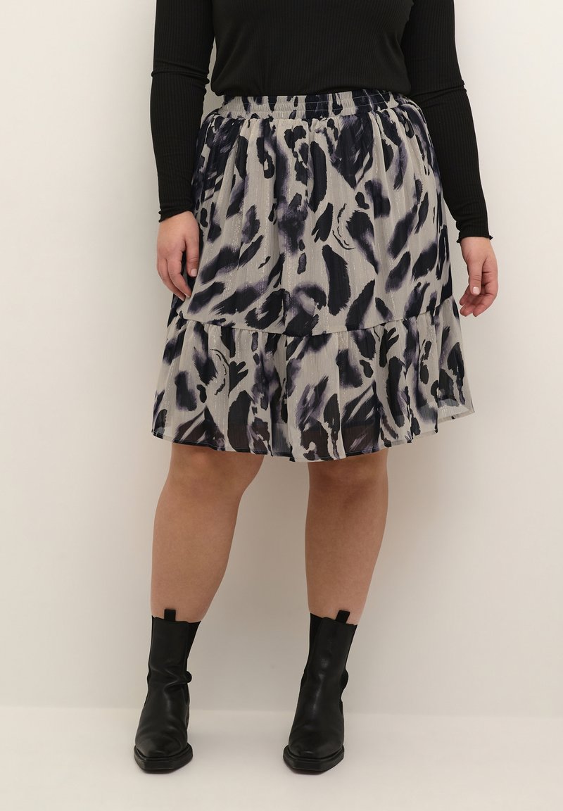 Jupe multi-couches multicolore en gris clair avec des motifs abstraits noirs et violets. Taille élastique et tissu léger. Bottines noires visibles.