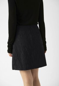 Jupe noire texturée avec une forme légèrement évasée et un motif froissé subtil, associée à un haut noir à manches longues ajusté.
