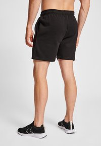 Schwarze Sportshorts mit einem elastischen Bund, geradem Schnitt und atmungsaktivem Stoff. Kombiniert mit schwarz-weißen Sportschuhen.