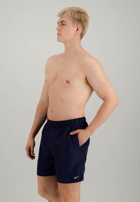 Shorts sportivi blu navy con cintura elastica e tasche laterali, dotati di un logo bianco sul lato sinistro. Il modello è in posizione di profilo.