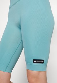 Niebieskie, elastyczne szorty sportowe o strukturze ryżowej, długości do połowy uda, z czarną metką Adidas po lewej stronie w pobliżu krawędzi.